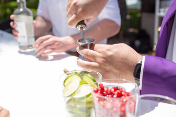 A bartender prepares a cocktail on the counter, pouring liquor bottle alcohol into a jigger.