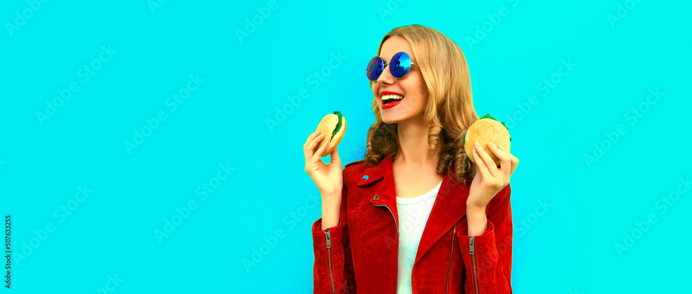 Wall mural portrait of stylish happy smiling young woman with tasty big burger fast food on blue background, bl