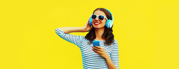 Portrait of smiling young woman in headphones listening to music with smartphone on yellow...
