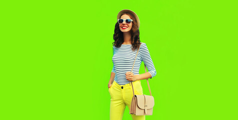 Portrait of happy smiling stylish young woman posing wearing handbag, striped t-shirt and summer straw round hat on green background, blank copy space for advertising text