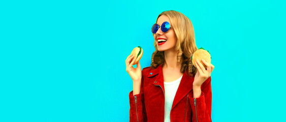Portrait of stylish happy smiling young woman with tasty big burger fast food on blue background,...