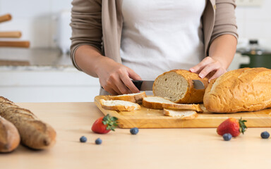 Selective focus woman or wife hand holding knife, cutting bread in cozy home kitchen in morning,...