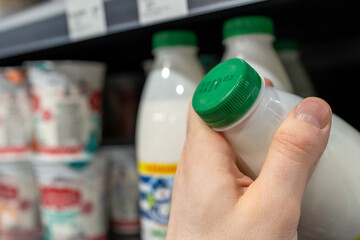 Buyer checks expiration date of dairy product before buying it. Hand holding milk bottle in supermarket. - obrazy, fototapety, plakaty