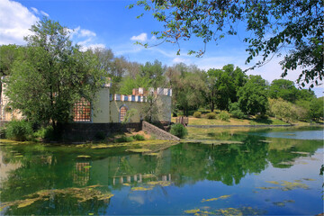 An old building in the form of a castle on an island in the middle of a pond.