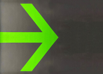direction arrow on a black wall, green direction arrow on a black background for orientation on a...