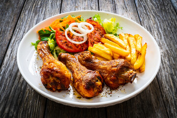 Barbecue chicken drumsticks with chips and greens on wooden table
