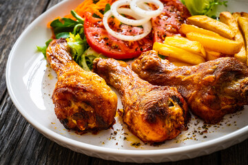 Barbecue chicken drumsticks with chips and greens on wooden table
