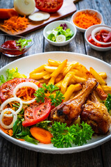 Barbecue chicken drumsticks with chips and greens on wooden table
