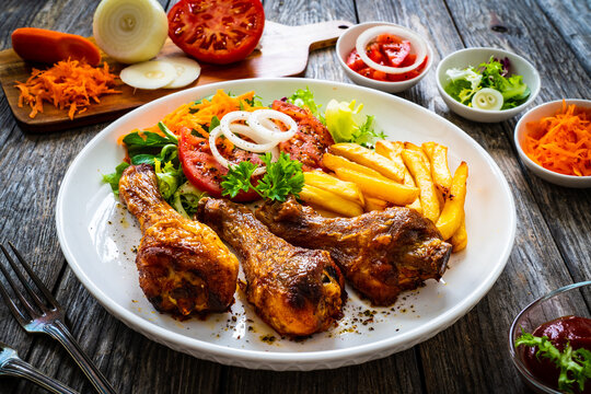 Barbecue chicken drumsticks with chips and greens on wooden table
