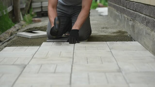 Man laying paving tiles on the floor using a rubber mallet and level