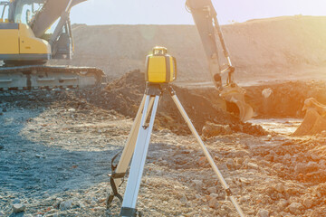 Rotating laser surveying equipment set on construction site with excavator digging foundation in...