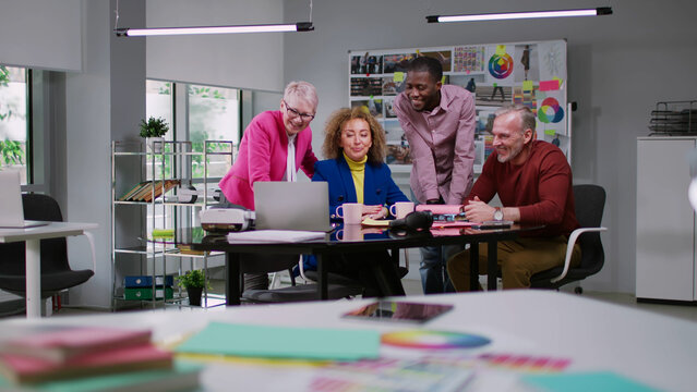 Multiethnic fashion magazine team discuss ideas looking at laptop screen in creative office