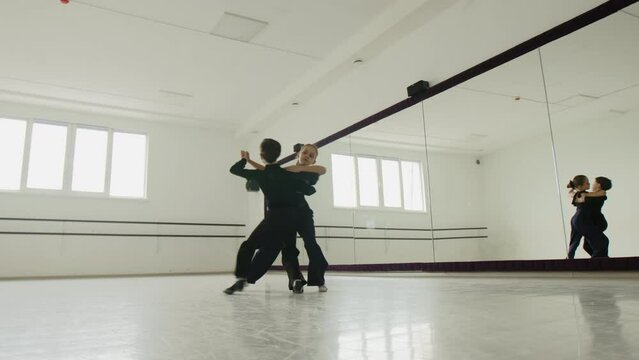 Choreography lesson with a boy and girl in a dancing hall. Little boy and girl waltzing together near the mirror. Pair wear black form. High quality 4k footage