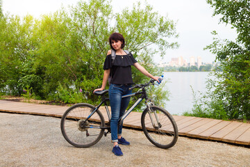 Fototapeta na wymiar A happy female tourist with a backpack rides a bicycle park along the river.