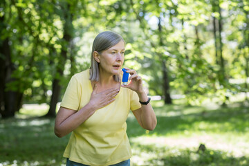 Seasonal allergies. An older woman in the park, in nature, has difficulty breathing, uses an inhaler. sneezes and coughs into a handkerchief. Has allergies, suffocates - obrazy, fototapety, plakaty