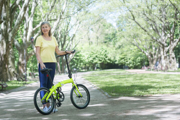 Active lifestyle. Senior beautiful woman walks in the park, rides a bike. He stands with a bicycle in his hands, looks at the camera, smiles.