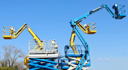 Group of work aerial platforms,  cherry pickers and scissor lifts models, against blue sky.