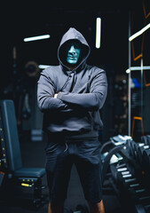 Strong lifestyle person holding in fitness club. Man in black hoodie standing in dark gym hall.