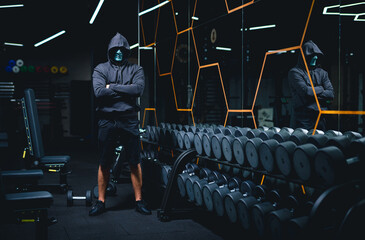 Man in black hoodie standing in dark gym hall. Strong lifestyle person holding in fitness club.