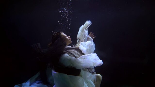 a brunette with long hair hovers with canvases of light fabric in dark water and moves hands. profile view