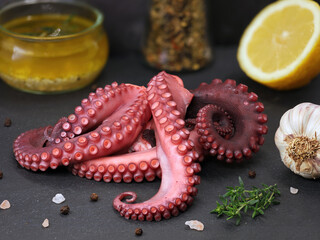 cooked octopus tentacles on black slate plate served with spices, garlic, lemon and olive oil