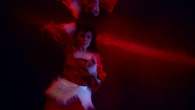 a woman with dark long hair and in a New Year's costume floats in dark water and is reflected in the surface. red light. the middle plan