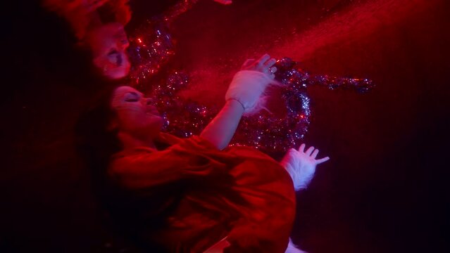 portrait of a brunette with long hair in dark water. the woman moves hands beautifully with tinsel and is reflected in the surface. red light. the middle plan