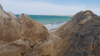 Fototapeta na wymiar Tas de gros rochers sur la belle plage de Plouédern en Bretagne, avec un mer bleu turquoise, de la végétation maritime verte et des flaques d'eau, et des vagues