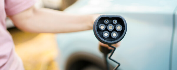 Unrecognizable Asian woman holding AC type 2 EV charging connector at EV charging station.