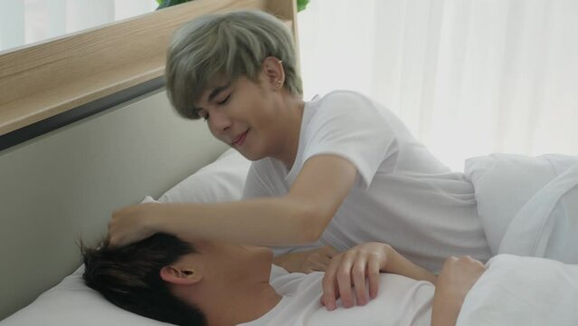Young Asian gay couple teasing in bed, kissing, touching hair, patting, looking at each other, making eyes contact, smiling, laughing, in the morning. Happy LGBT, passionated love, lifestyle concept.