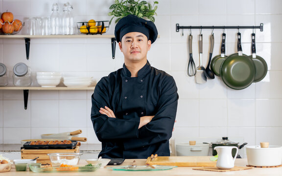 Portrait handsome professional Japanese male chef wearing black uniform, hat, crossing arms, cooking, preparing ingredients for takoyaki, smiling, standing in kitchen. Restaurant, Hotel Concept.