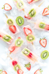 Refreshing strawberry kiwi popsicles scattered around on a bed of ice.