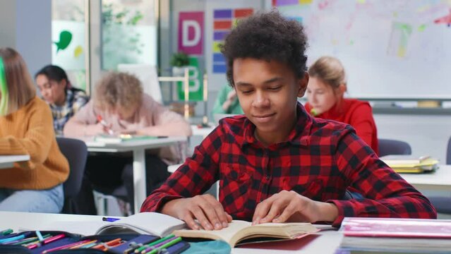 African-American teenage boy read book sitting at desk in classroom