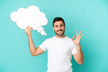 Young handsome caucasian man isolated on blue background holding a thinking speech bubble and doing OK sign