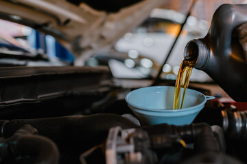In the car service center the mechanics are filling the engine with new oil for engine maintenance.