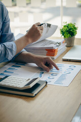 Young businessman working in piles of paper files, searching for information, business reports and piles of unfinished papers on laptop computer desk in modern office, portrait photo.