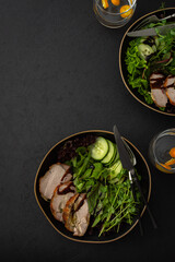 Hearty delicious lunch, fresh salad with cucumbers and microgreens of peas and with stewed pork, top view of the dark table with food
