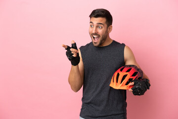 Young cyclist man isolated on pink background pointing finger to the side and presenting a product - obrazy, fototapety, plakaty