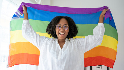 African American young woman smiling and raising and waving the LGBT flag in the air in...