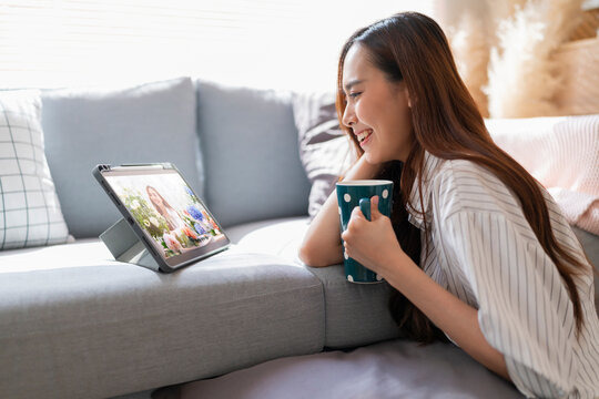 asian attractive female wear casual cloth home isolate quarantine enjoy watching streaming bradcast online movie program via tablet on floor next to sofa in living room home interior cosy background