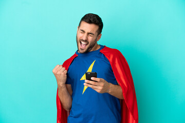 Super Hero caucasian man isolated on blue background with phone in victory position