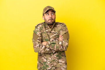 Military man isolated on yellow background making doubts gesture while lifting the shoulders