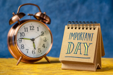 important day reminder note in a desktop calendar with an alarm clock - obrazy, fototapety, plakaty