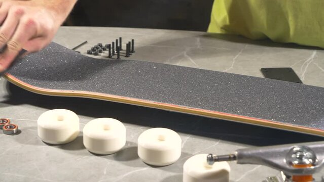 CLOSE UP: Young male person smoothing the cut edges of skateboard griptape with leftover scraps. Unrecognizable young man applying finishing touches to a new skateboard deck to get a clean, soft edge.