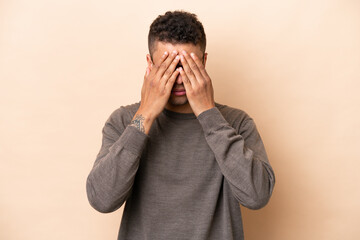 Young Brazilian man isolated on beige background covering eyes by hands