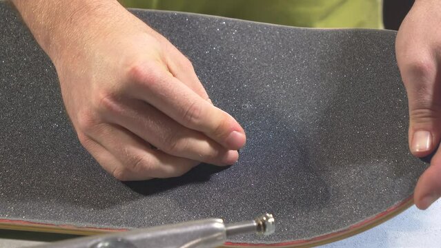 CLOSE UP: Young man inserting the bolts through truck holes on skateboard deck from above. Unrecognizable male person installing bolts through griptape marks to screw skateboard trucks to the deck.