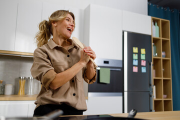 Happy housewife woman singing with a wooden spatula in the kitchen at home