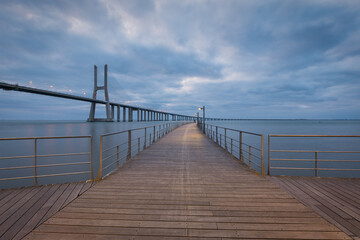 Fototapeta premium Vasco da Gama bridge and pier over tagus river in Lisbon, Portugal, at dawn, with a cloudy sky.