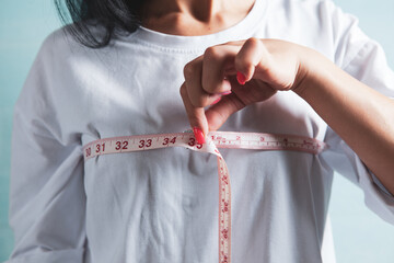 Slim woman measures her breast with a measuring tape