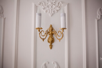 antique golden candlestick on white wall. Retro copper candlestick hanging on the wall. Vintage golden candlestick with light bulbs. Gold wall candle holder on a white background. closeup photo